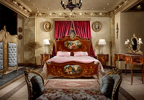 An Awe inspiring French Louis XV and Vernis Martin style ormolu-mounted, veneer and marquetry inlaid four pieces Royal Bedroom Set comprising of one bed, one coiffeuse and two nightstands, the bed is adorned with exquisitely chased Rococo style ormolu mounts of swaging blossoming garlands, large ormolu chutes on corners and central pierced ormolu crest with central portraits of beautifully hand painted romantic court scenes on headboard and footboard amidst floral marquetry inlays; the coiffeuse is marquetry inlaid as well and has an ormolu Rocaille style cartouche-shaped bevelled mirror supported by ormolu pierced scrolled-acanthus uprights and flanked to each side by four lighting candelabrum.